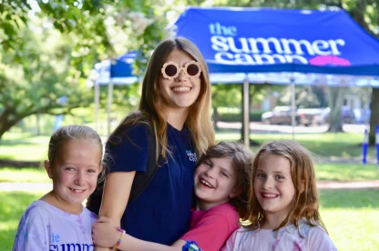a staff member with sunglasses on hugging the kids at summer camp
